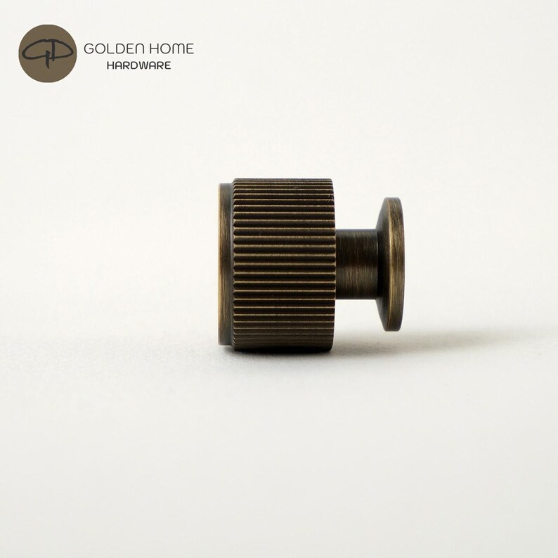 May include: A bronze-colored cabinet knob with a cylindrical, ridged body and a circular base. The knob has a vintage aesthetic and is likely made of metal. The logo "GOLDEN HOME HARDWARE" is in the upper left corner.