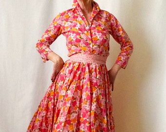 Puede incluir: Un vestido de estampado floral rosa y naranja con una camisa de manga larga y una falda completa. El vestido tiene un cinturón blanco con lunares rosas.