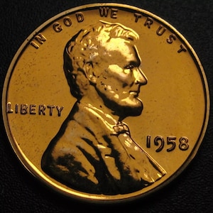 May include: A close-up of a gold-coloured 1958 Lincoln penny. The coin features a profile of Abraham Lincoln, the word "LIBERTY", and the phrase "IN GOD WE TRUST". The year "1958" is also visible.