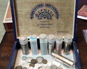 May include: A blue wooden cigar box with a gold latch. The box is open and contains a collection of silver coins in clear plastic tubes. The box is labeled "H. Upmann Nicaragua AJ Fernandez Heritage Toros 6 x 54".