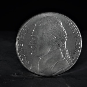 May include: A silver US nickel coin with the profile of Thomas Jefferson on the obverse side. The coin reads "LIBERTY 2004" and "IN GOD WE TRUST" on the obverse side.