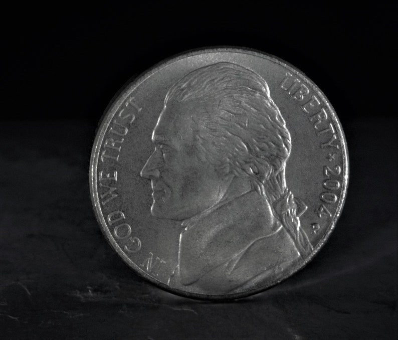 May include: A silver US nickel coin with the profile of Thomas Jefferson on the obverse side. The coin reads "LIBERTY 2004" and "IN GOD WE TRUST" on the obverse side.