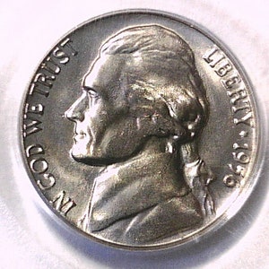 May include: A silver nickel coin with a profile of a man, inscribed with "LIBERTY" and "IN GOD WE TRUST". The coin also shows the year "1956".