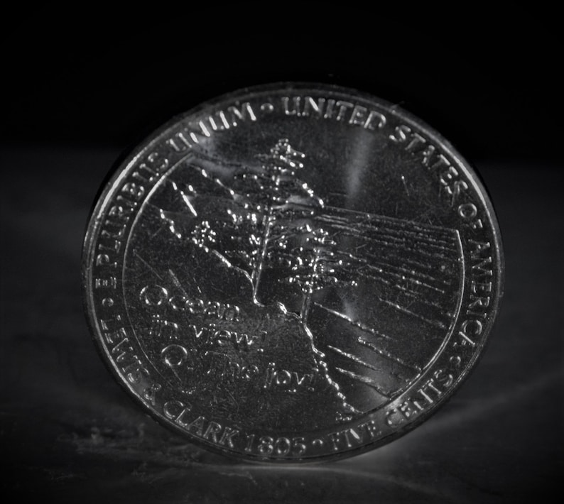 May include: A silver United States quarter dollar coin with the words "E Pluribus Unum" and "United States of America" around the edge. The coin features a depiction of the Lewis and Clark Expedition with the words "Lewis & Clark 1805-1806" and "Great Western View" on the coin.