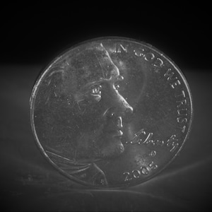 May include: A silver US penny with the profile of Abraham Lincoln and the inscription "In God We Trust" on the obverse side. The year 2005 is visible on the coin.