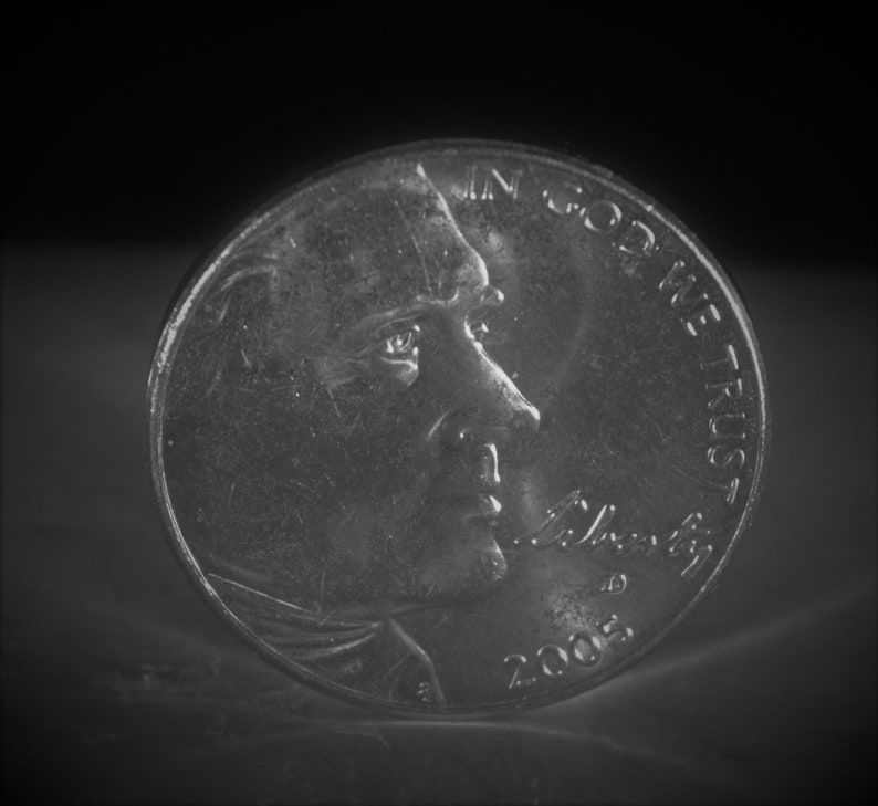 May include: A silver US penny with the profile of Abraham Lincoln and the inscription "In God We Trust" on the obverse side. The year 2005 is visible on the coin.