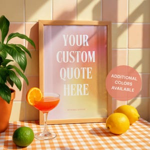 May include: A framed print with the text "YOUR CUSTOM QUOTE HERE" in white, set against a gradient background of pink, orange, and yellow. A cocktail with an orange slice garnish sits in front of the frame, along with a lime and lemons.