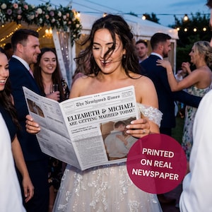 Może przedstawiać: Panna młoda trzyma gazetę zatytułowaną "The Newlywed Times" z nagłówkiem "ELIZABETH & MICHAEL ARE GETTING MARRIED TODAY!". Gazeta zawiera zdjęcie pary. Tekst "PRINTED ON REAL NEWSPAPER" znajduje się na różowym okręgu.