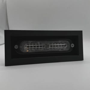 May include: A rectangular black light fixture with a clear, segmented light source. The light source is encased in a clear plastic and secured with two screws. The fixture is designed for recessed mounting.