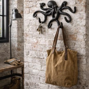 May include: Black cast iron octopus wall hook holding keys and a brown tote bag. The octopus design has multiple curved arms and is mounted on a brick wall. The tote bag has brown leather handles.