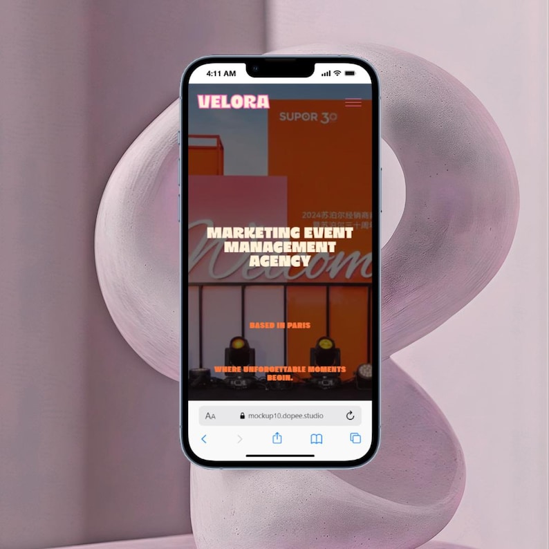 May include: A smartphone displaying a website for Velora, a marketing event management agency based in Paris. The screen shows orange and white text over an orange background, including the phrases Marketing Event Management Agency and Where Unforgettable Moments Begin.