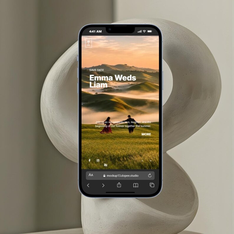 May include: A smartphone displays a wedding announcement with the text "Emma Weds Liam" over a scenic landscape. The website address "mockup13.dopee.studio" is visible at the bottom. The phone is positioned in front of a neutral-toned, abstract sculpture.
