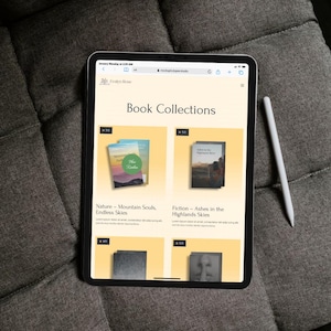 Pu&ograve; includere: Un tablet mostra un sito web intitolato "Book Collections" con copertine di libri. Il sito web presenta libri come "Nature - Mountain Souls, Endless Skies" e "Fiction - Ashes in the Highlands Skies". Una penna bianca &egrave; appoggiata a destra.