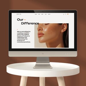 May include: A desktop computer displaying a website with the text "EVALYN" and "Our Difference." The website features a photo of a person and text about beauty and nature. The computer sits on a white table with a brown background.
