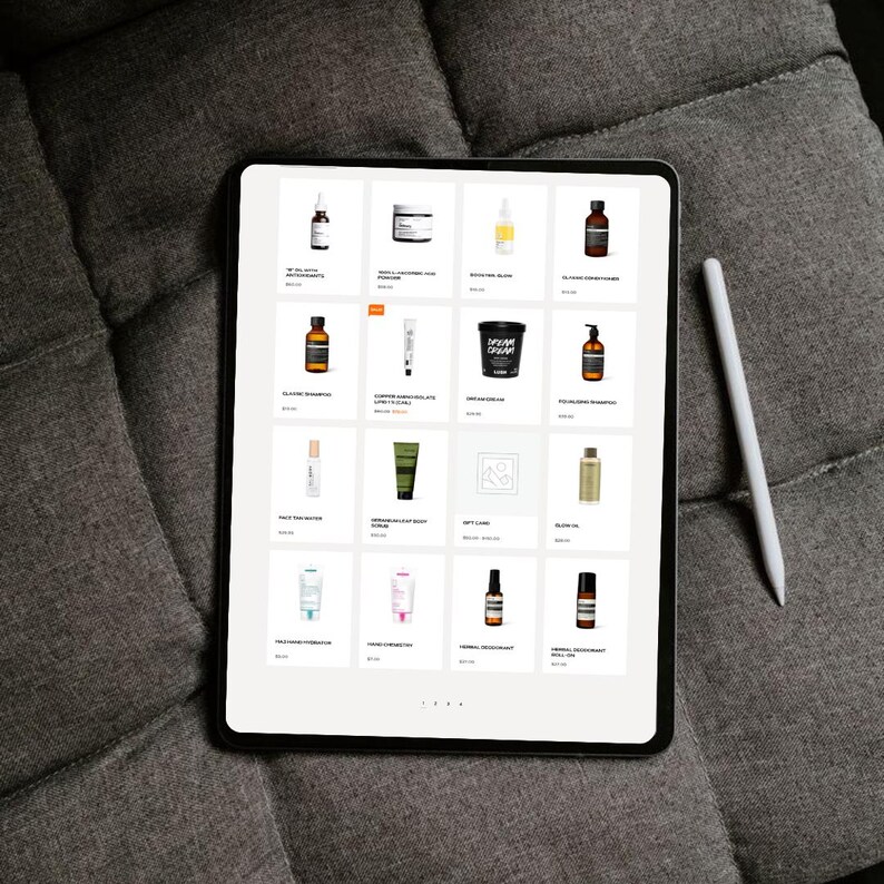 May include: A digital tablet displaying a grid of various skincare and beauty products. The products are in bottles, jars, and tubes, with labels visible. A white stylus rests beside the tablet on a gray upholstered surface.