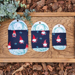 May include: Three different sizes of navy blue fabric cup cozies with a Christmas gnome pattern. The cozies are on white card stock with the text "Crafty Cozy Way" printed on them.