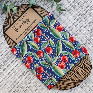 May include: A blue fabric pouch with a white polka dot pattern and a cherry print. The pouch has the text "Crafty That Way Yarn Cozy" and a quote by Albert Einstein: "Creativity is intelligence having fun."