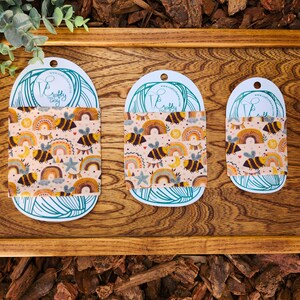 May include: Three different sizes of reusable food wraps with a bee and rainbow pattern. The wraps are made of beeswax, jojoba oil, and tree resin. The wraps are a sustainable alternative to plastic wrap.