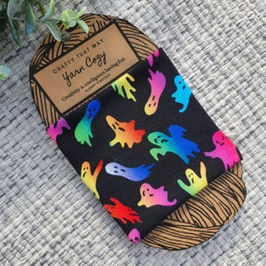May include: A black fabric band with a rainbow ghost pattern. The band is packaged on a brown cardboard backing with the text "Crafty That Way Yarn Cozy" and a quote from Albert Einstein: "Creativity is intelligence having fun."