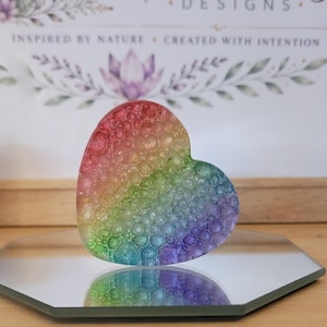 May include: A heart-shaped object with a textured, bubble-like surface featuring a vibrant rainbow gradient of red, orange, yellow, green, blue, and purple colors. The piece is translucent and displays a distinct pattern of raised circular cells.