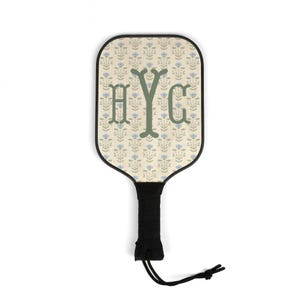 Könnte beinhalten: Ein Pickleball-Schläger mit einem floralen Muster in Beige und Blau. Der Schläger hat die Buchstaben "HYG" in Grün. Der Griff ist schwarz mit einer schwarzen Kordel befestigt. Der Schläger ist für den Freizeitgebrauch konzipiert.