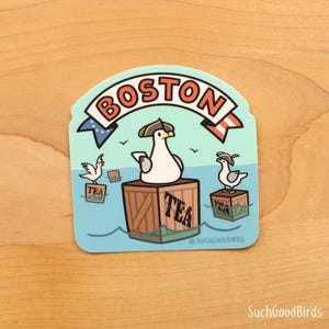 May include: A blue and white sticker with a cartoon seagull wearing a captain's hat and holding a tea box. The seagull is standing on a wooden crate with the word "TEA" printed on it. The sticker also features the word "BOSTON" in a red and white banner.