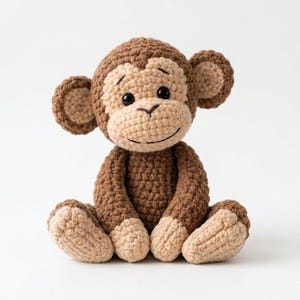 Peut inclure: Une poupée singe au crochet faite à la main, dans les tons marron et beige. Le jouet en peluche présente un visage souriant, de grandes oreilles et des coutures détaillées. Le singe est assis droit, montrant ses bras, ses jambes et ses pieds.
