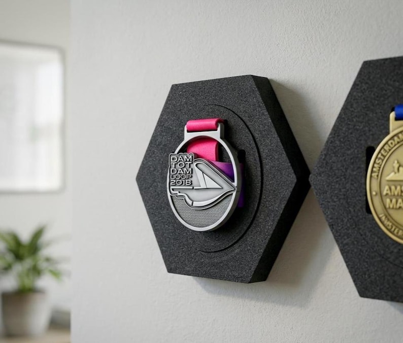 Pu&ograve; includere: Un espositore di medaglie esagonale nero con una medaglia d'argento con la scritta "DAM TOT DAM LOOP 2018" e un nastro rosa. La medaglia &egrave; posta su uno sfondo grigio scuro.