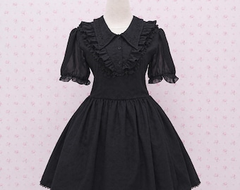 Pode incluir: Um vestido preto com gola pontiaguda com bordados intrincados, mangas curtas bufantes com punhos franzidos e um corpete abotoado. O vestido tem uma cintura ajustada e uma saia rodada com bainha franzida, tudo feito em tecido preto sólido.
