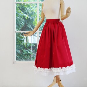 May include: A red skirt with a white lace trim. The skirt is gathered at the waist and has a full, flowing silhouette.