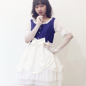 May include: A white dress with lace trim and a blue bodice. The dress has a layered skirt and a bow at the waist. The person is wearing white lace gloves and red shoes.