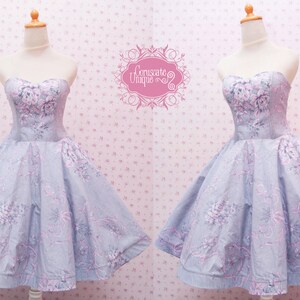 May include: A strapless dress featuring a light blue fabric with a pink and white floral pattern. The bodice is fitted with a sweetheart neckline, and the skirt is flared. The text Coruscate Unique is visible in a pink decorative frame.