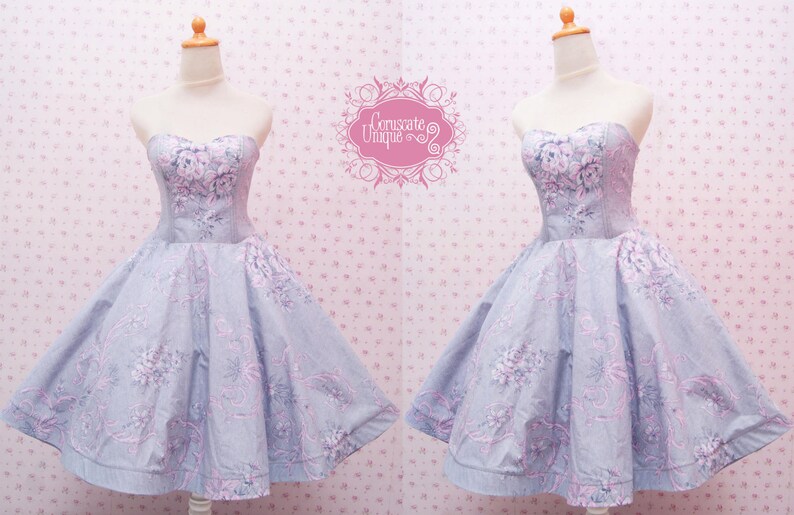 May include: A strapless dress featuring a light blue fabric with a pink and white floral pattern. The bodice is fitted with a sweetheart neckline, and the skirt is flared. The text Coruscate Unique is visible in a pink decorative frame.