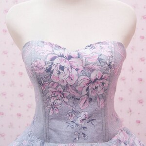 May include: A strapless bodice dress featuring a grey fabric base with a printed pattern of large pink and dark grey floral motifs. The garment has a sweetheart neckline and vertical seam detailing along the front, extending into a full skirt.