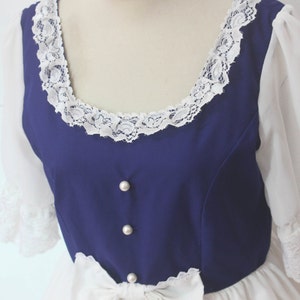 May include: A white dress with a blue bodice and white lace trim. The bodice has pearl buttons and a white bow at the waist.