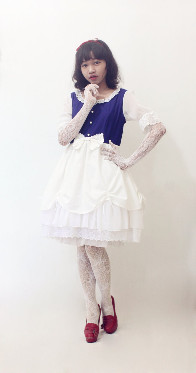 May include: A white dress with lace trim and a blue bodice. The dress has a layered skirt and a bow at the waist. The person is wearing white lace gloves and red shoes.