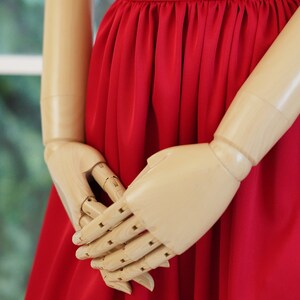 May include: A wooden mannequin wearing a red dress with a gathered skirt.