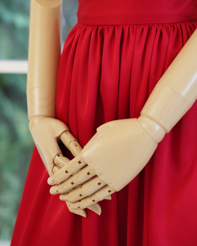 May include: A wooden mannequin wearing a red dress with a gathered skirt.