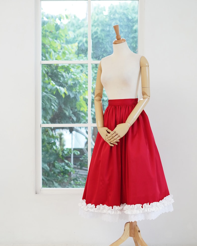 May include: A red skirt with a white lace trim. The skirt is on a mannequin and has a gathered waist.