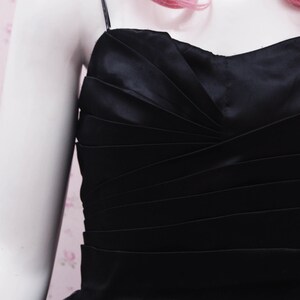 May include: A black tulle and satin dress with a fitted bodice and a full skirt. The bodice has a gathered design and the straps are thin.