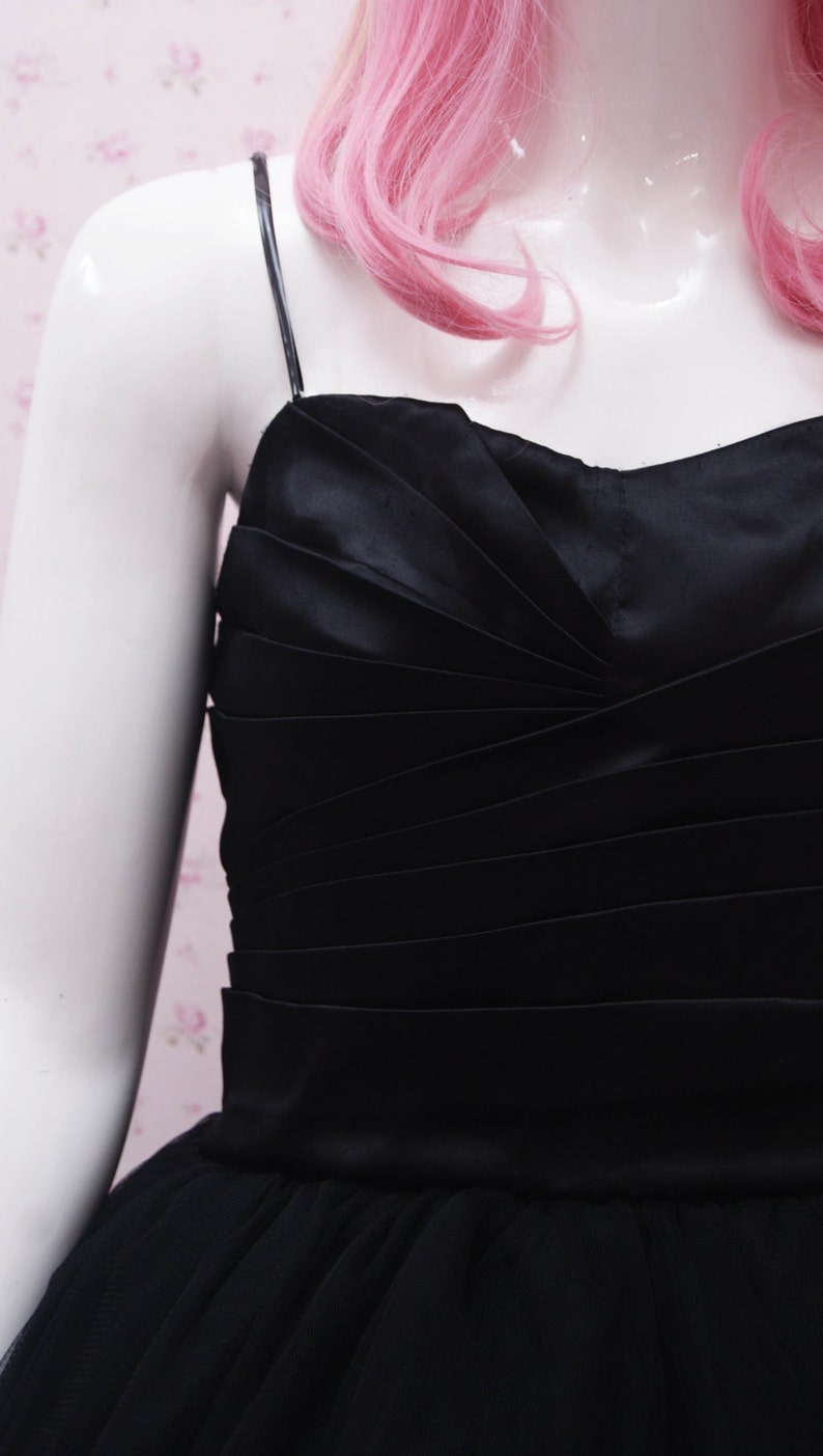 May include: A black tulle and satin dress with a fitted bodice and a full skirt. The bodice has a gathered design and the straps are thin.
