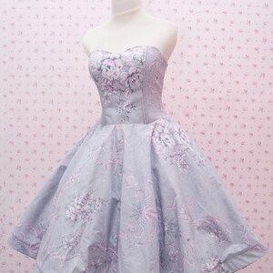 May include: A strapless dress featuring a light gray base color with a repeating floral and scrollwork pattern in shades of soft pink and darker gray. The bodice is fitted with a sweetheart neckline, transitioning into a full, flared skirt.