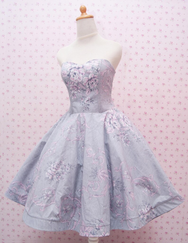 May include: A strapless dress featuring a light gray base color with a repeating floral and scrollwork pattern in shades of soft pink and darker gray. The bodice is fitted with a sweetheart neckline, transitioning into a full, flared skirt.