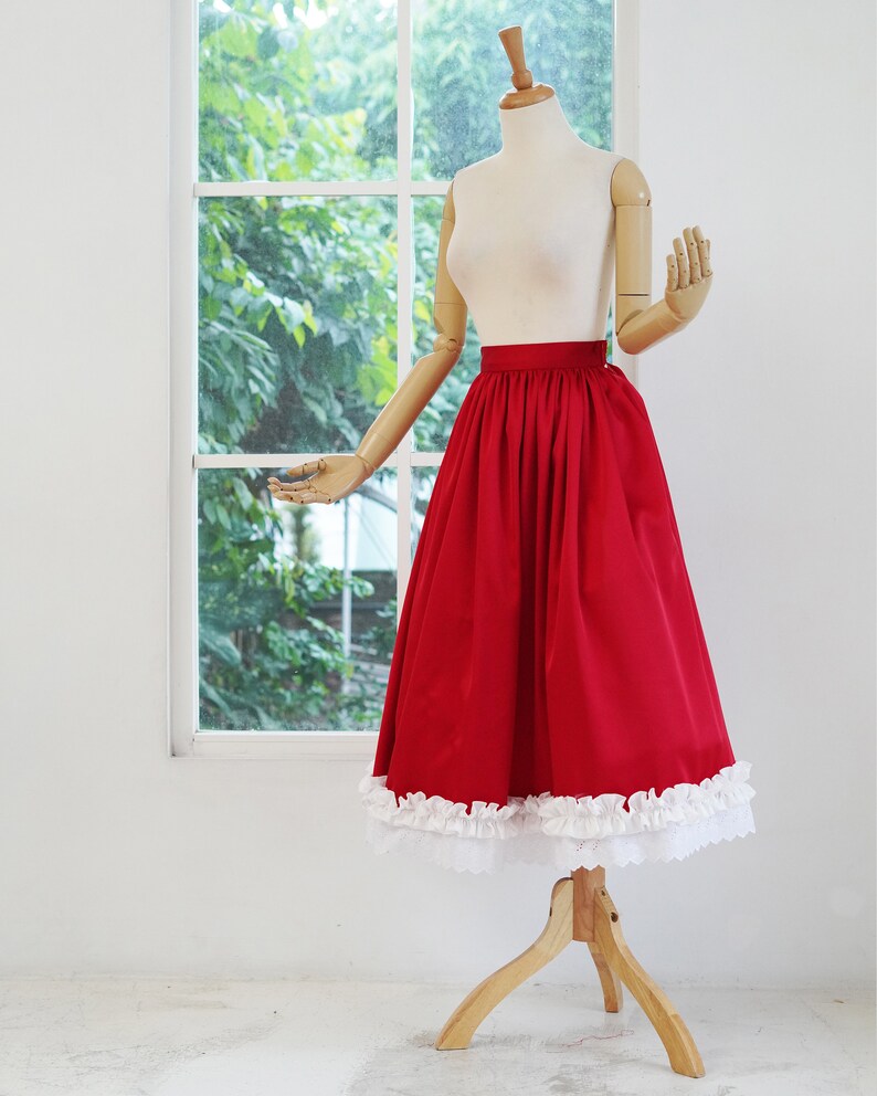 May include: A red skirt with a white lace trim. The skirt is gathered at the waist and has a full, flowing silhouette.