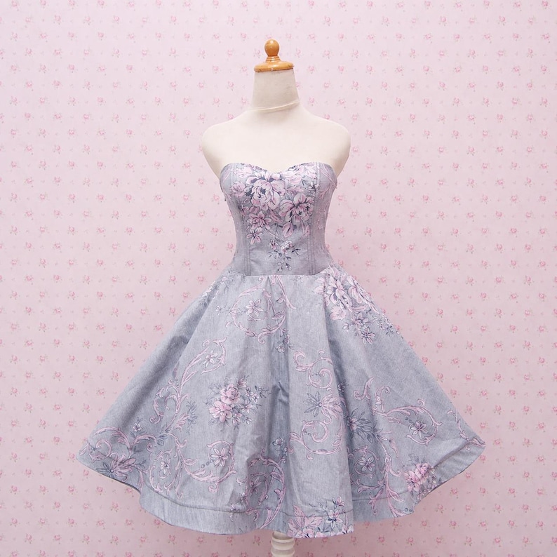 May include: A strapless knee-length dress in a light gray fabric featuring a repeating pattern of pink floral bouquets and swirling vine motifs. The bodice is fitted with vertical seams, transitioning into a full, flared skirt silhouette.