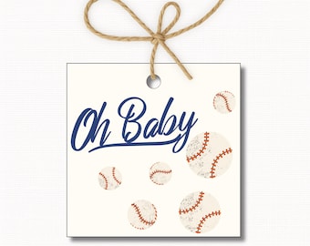 May include: A square, off-white tag with the words "Oh Baby" in navy blue script, and several baseballs. The tag is tied with a natural twine bow. The baseballs have red stitching.