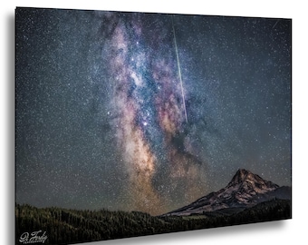 May include: A framed print of a night sky scene featuring the Milky Way galaxy, a shooting star, and a mountain range. The galaxy is a vibrant mix of blues, purples, and oranges, with a dark forest in the foreground.