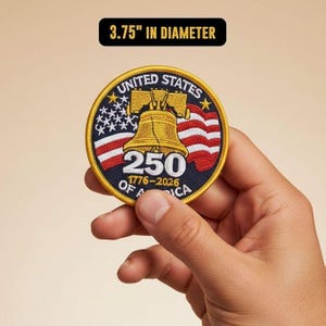 May include: Embroidered patch, 3.75 inches in diameter, featuring the Liberty Bell, American flag, and text "UNITED STATES 250 OF AMERICA 1776-2026". The patch has a gold border and is held in a hand.