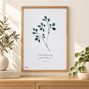 Op de afbeelding: Een ingelijste wandkunstprint met een aquarelillustratie van een donkergroene tak met bladeren, gecentreerd op een witte achtergrond. Onder de tak staat de tekst: Si Dios esta conmigo, ¿quien contra mi? Romanos 8:31. Een klein rood logo staat in de hoek.
