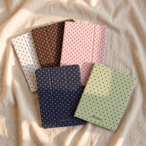 May include: Five rectangular tablet cases featuring a polka dot pattern in white, brown, pink, navy blue, and light green. The navy blue case is personalized with the name Gabriel, and the light green case is personalized with the name Aiden.